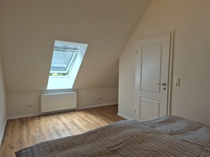 Una habitación con techo inclinado, tragaluz, radiador, puerta y cama con colcha a rayas.