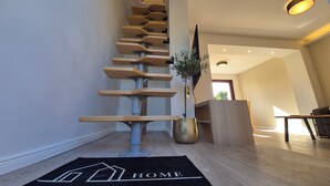 Moderni, ainutlaatuisella designilla varustettu portaikko, musta ovimatto, jossa on teksti »KOTI», ja kasvi nurkassa.