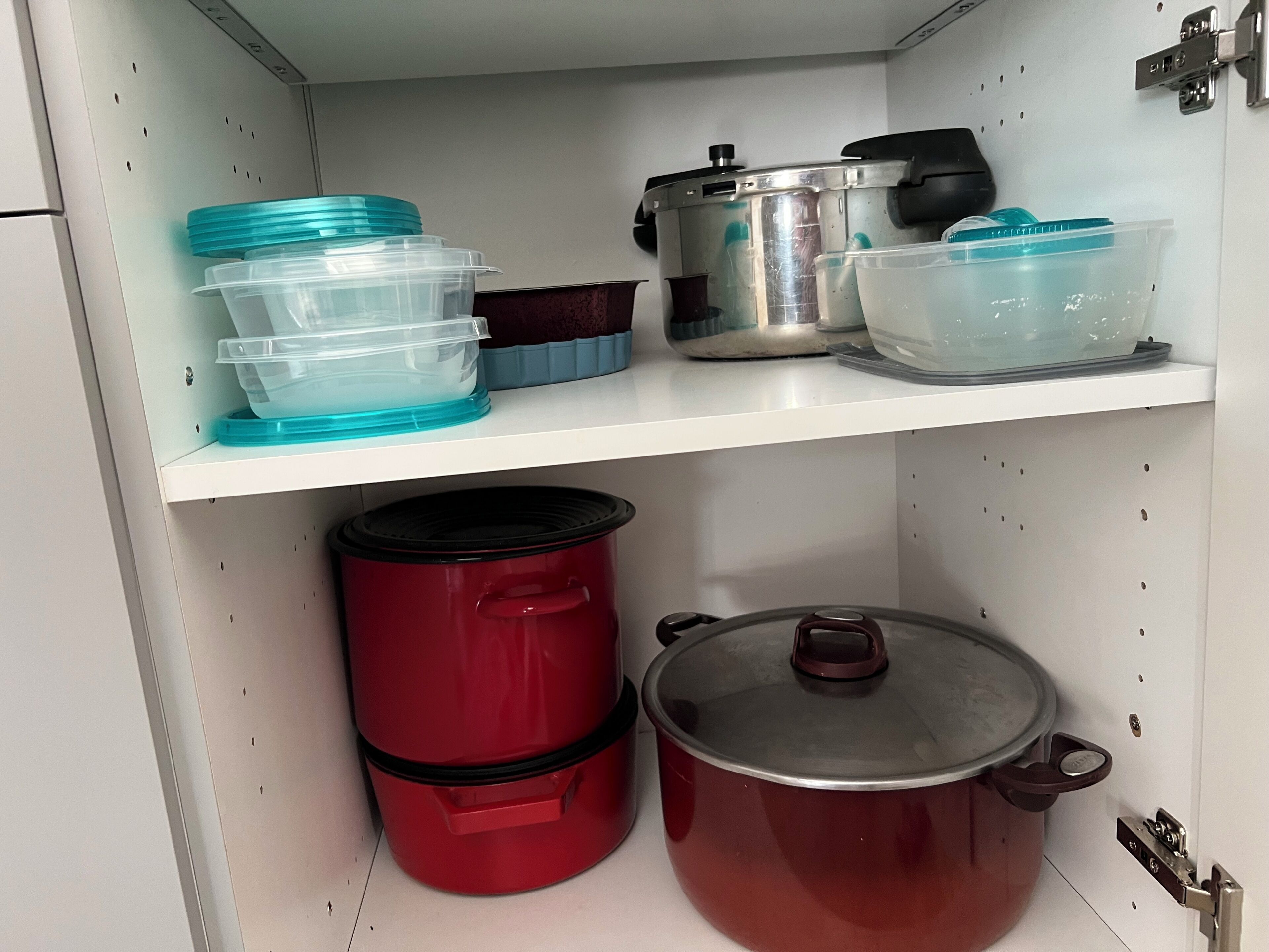 Een keukenkast met opbergplanken, gevuld met plastic bakken, een rode slowcooker en een roestvrijstalen pan.
