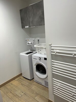 Ein Waschraum mit einer Frontlader-Waschmaschine und einem Trockner, einem Wäscheständer und einem Schrank darüber.
