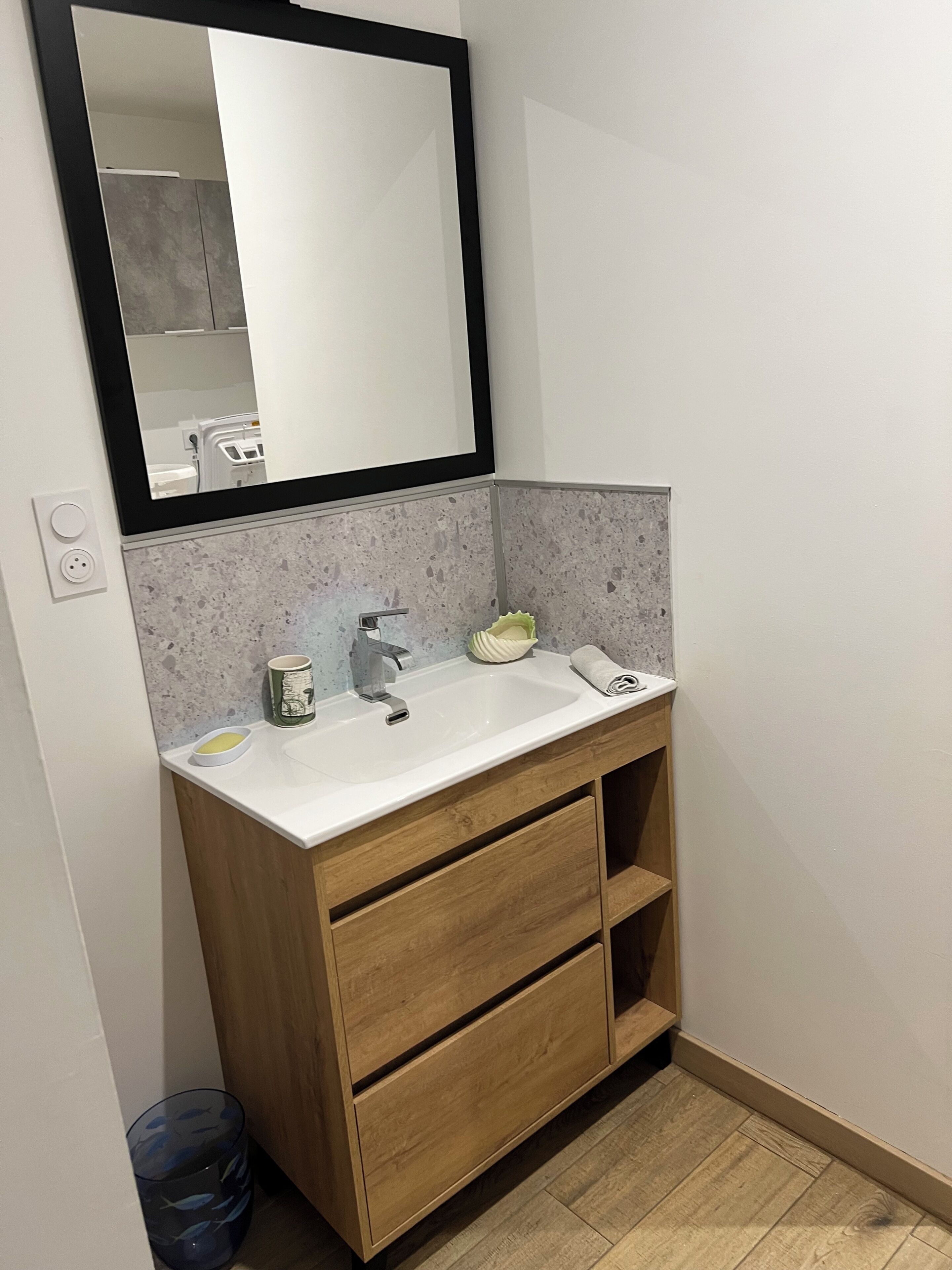 Een badkamer met een wit wastafel, houten opbergmeubel en een spiegel erboven.