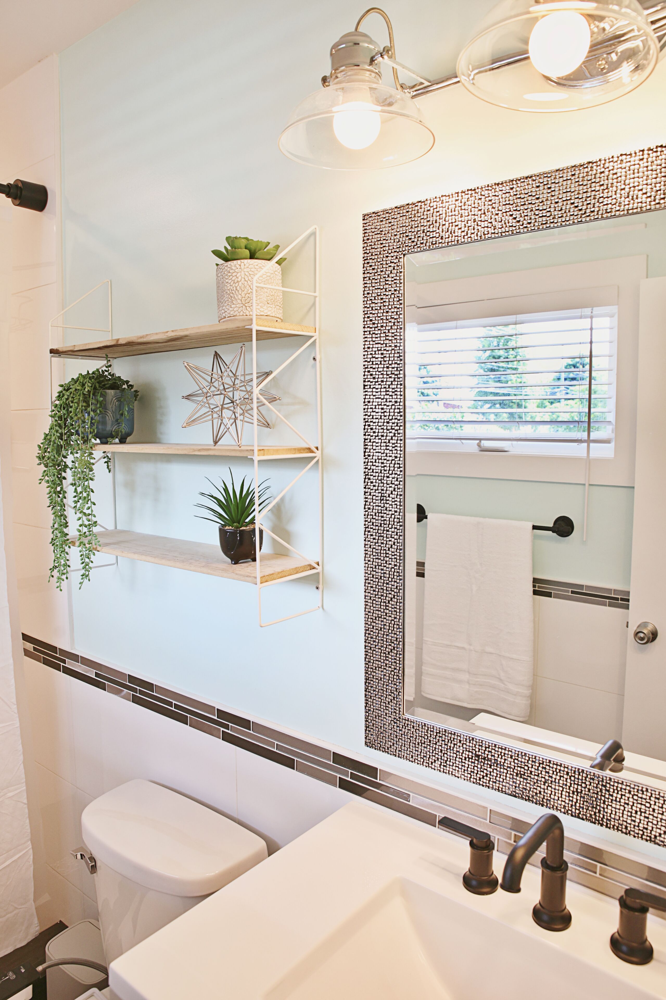 A bathroom with a toilet, sink, and mirror. There are shelves with plants and a decorative star.