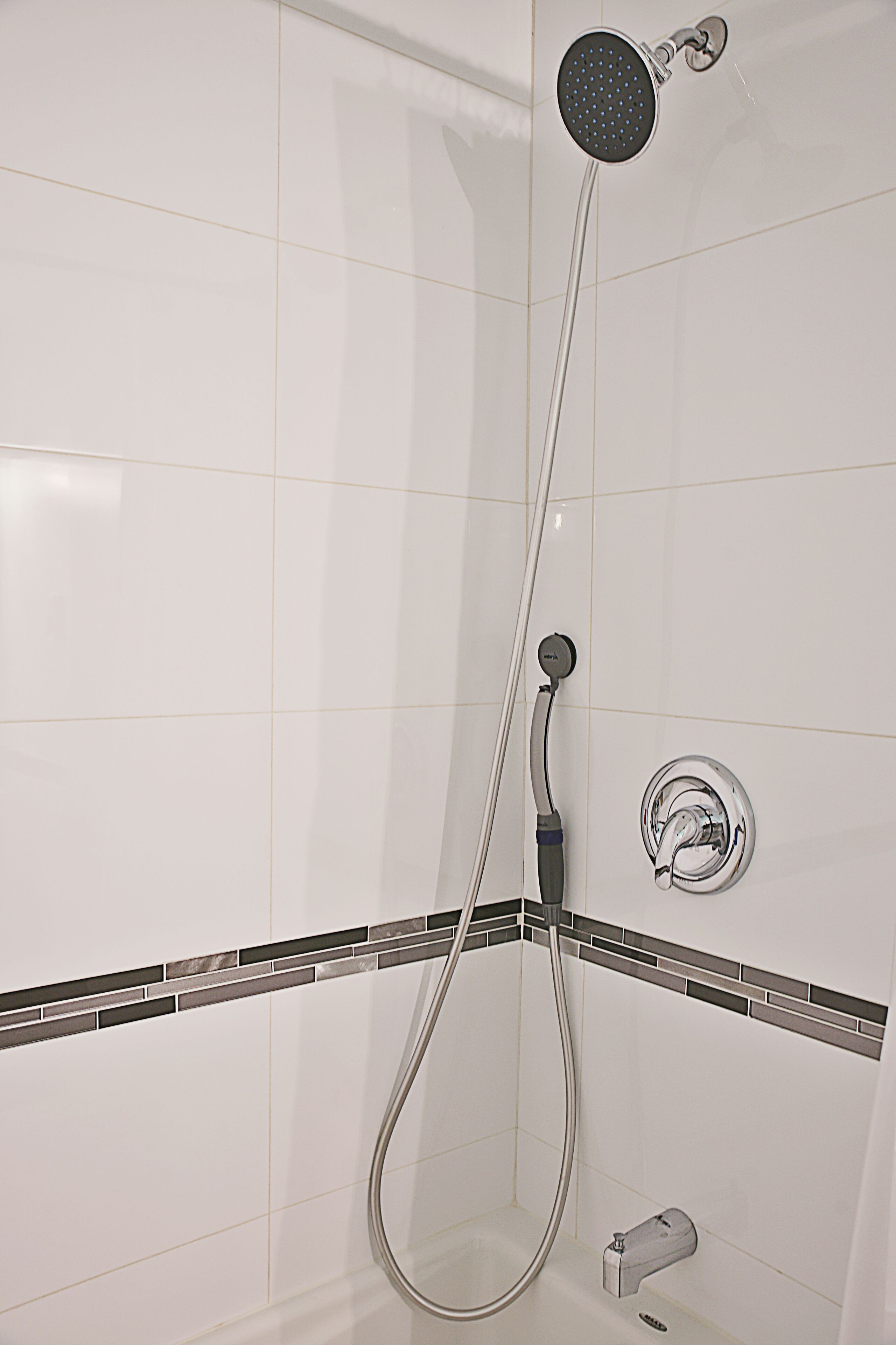 A shower with a handheld showerhead and a wall-mounted faucet.