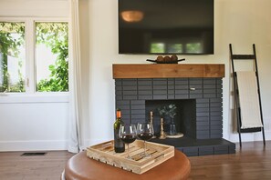 A modern living room with a fireplace, a wooden bench, and a tray with wine bottles and glasses. - Luma House - Poolside 4-bedroom retreat in Moncton (Moncton)
