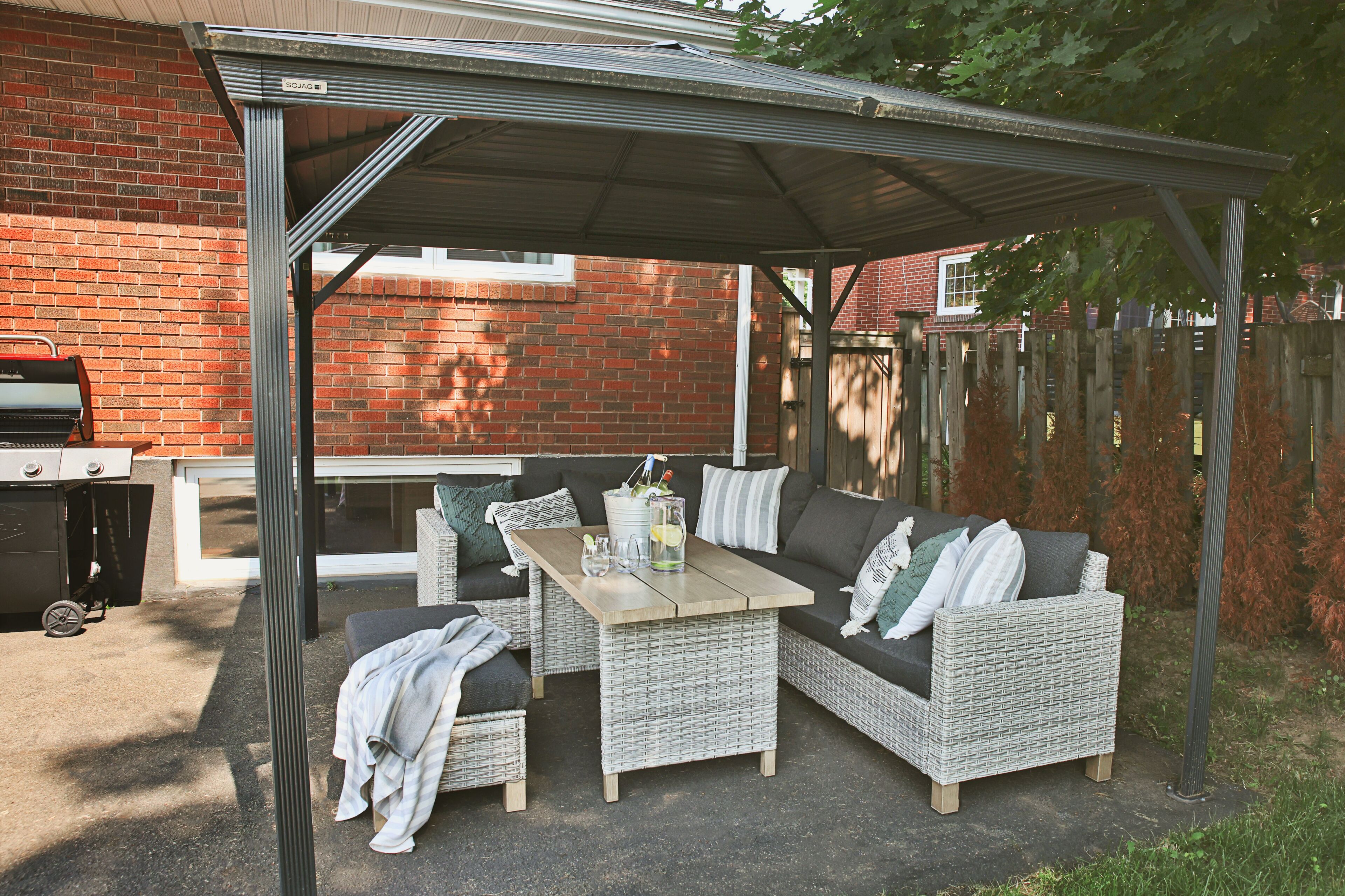 Une terrasse extérieure dotée d’un espace salon couvert, d’un barbecue et d’un mur de briques en arrière-plan.