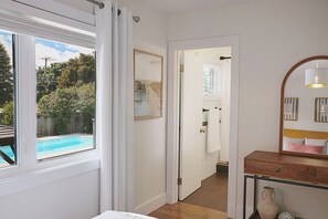 Une chambre avec vue sur une piscine, un meuble en bois, un miroir et une porte donnant sur une autre pièce.