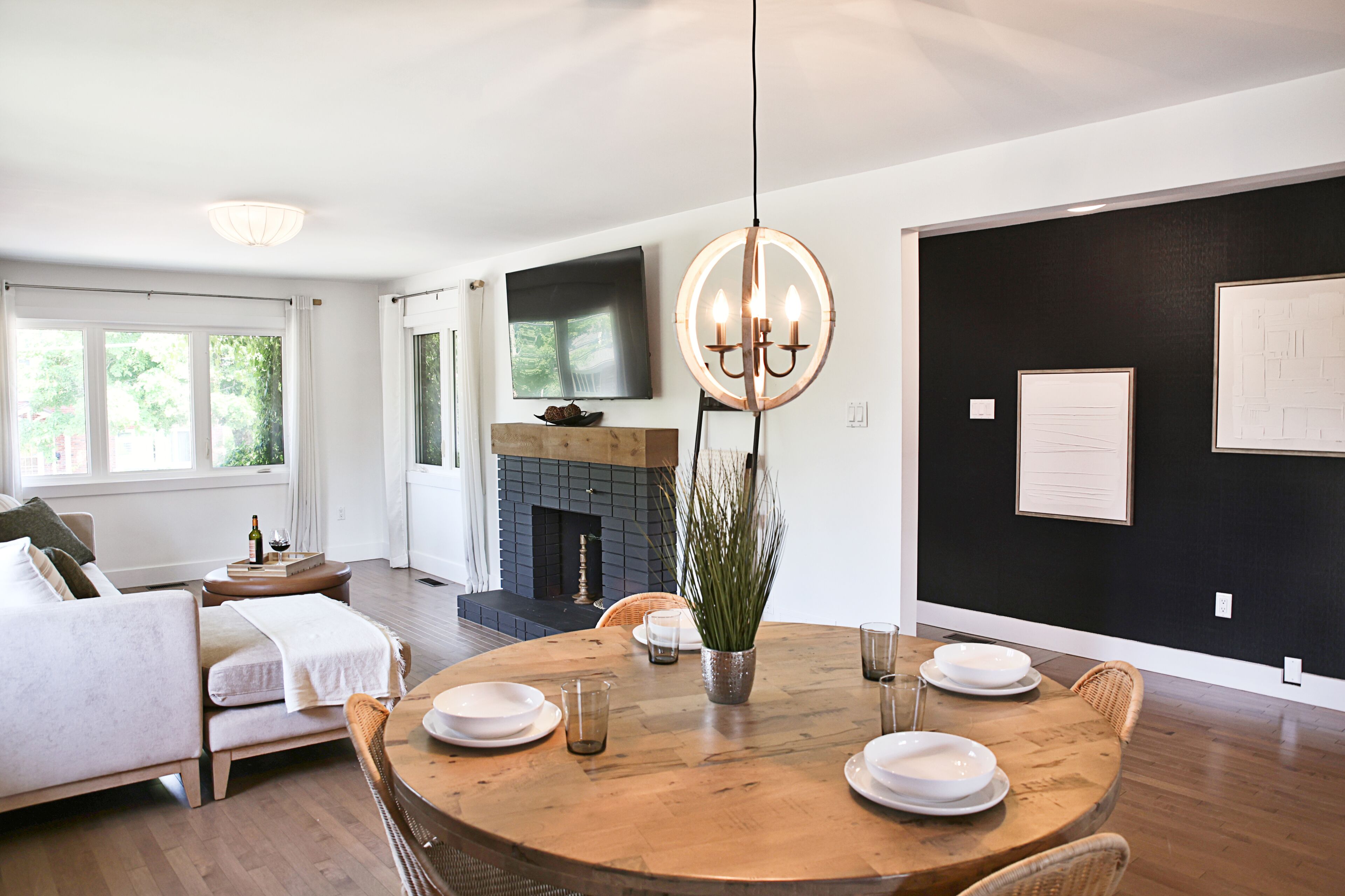 A modern living room with a fireplace, a dining area with a round wooden table, and a large flat-screen TV mounted on the wall.