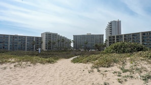 Um hotel à beira-mar com vários edifícios altos, caminhos de areia e alguma vegetação.