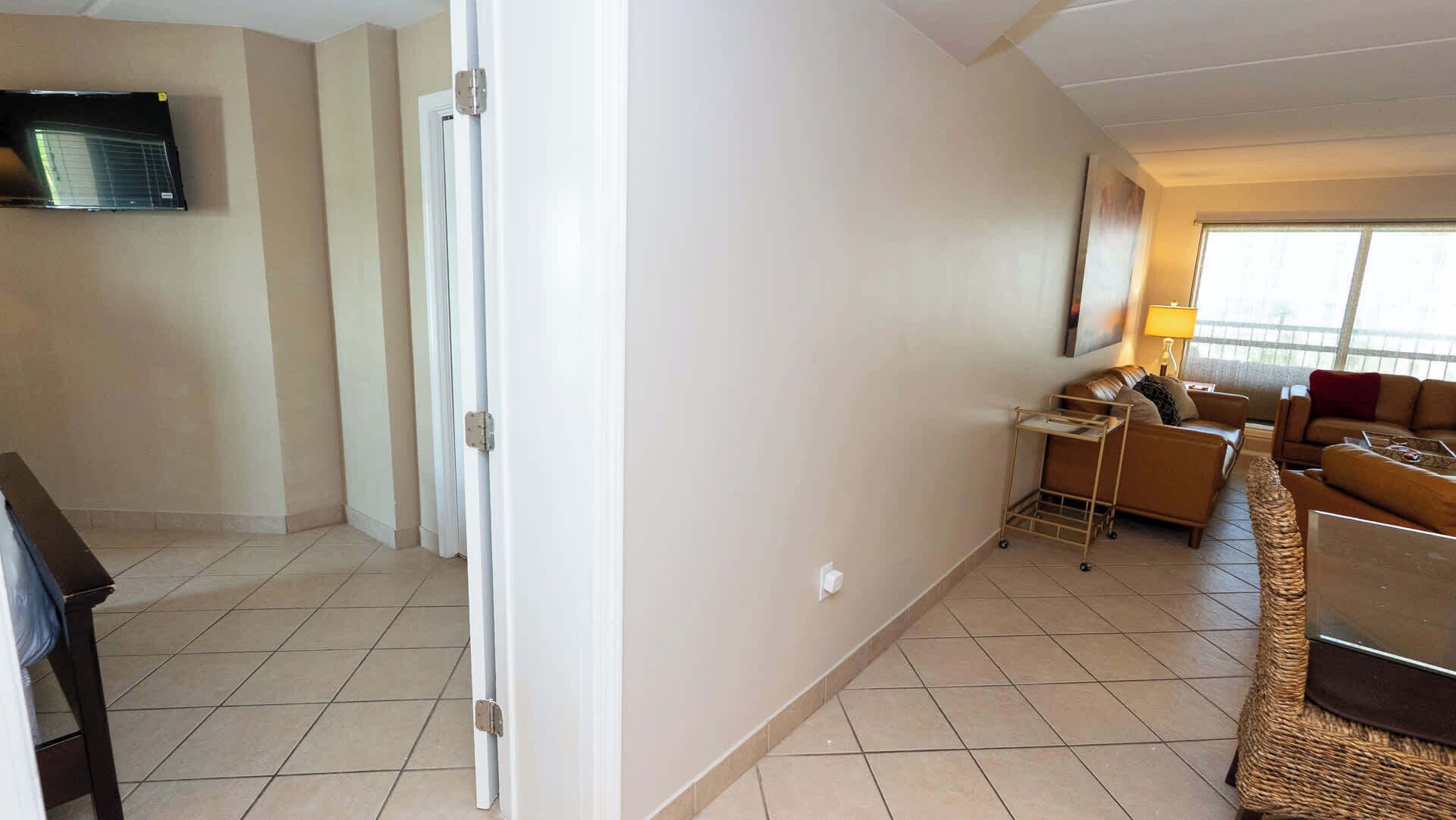 Une chambre d’hôtel équipée d’un téléviseur à écran plat fixé au mur, d’un canapé, d’une petite table et d’un fauteuil en osier.