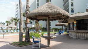 Ein Poolbereich eines Resorts mit Reetdachschirmen, Liegestühlen und einer Bar.