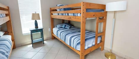 A bunk bed room with a lamp, a small table, and a window with blinds.