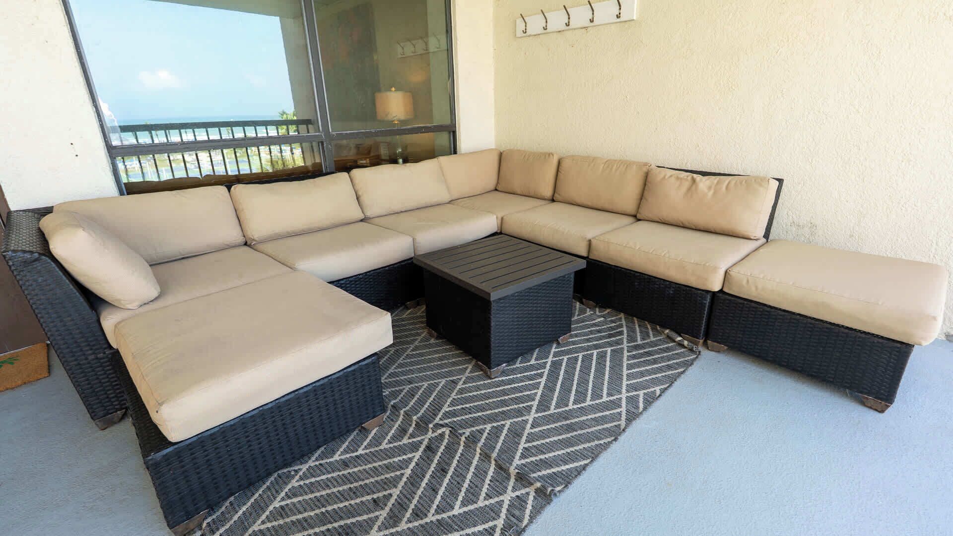 A sectional sofa with a matching ottoman and a woven coffee table, set on a patterned rug.