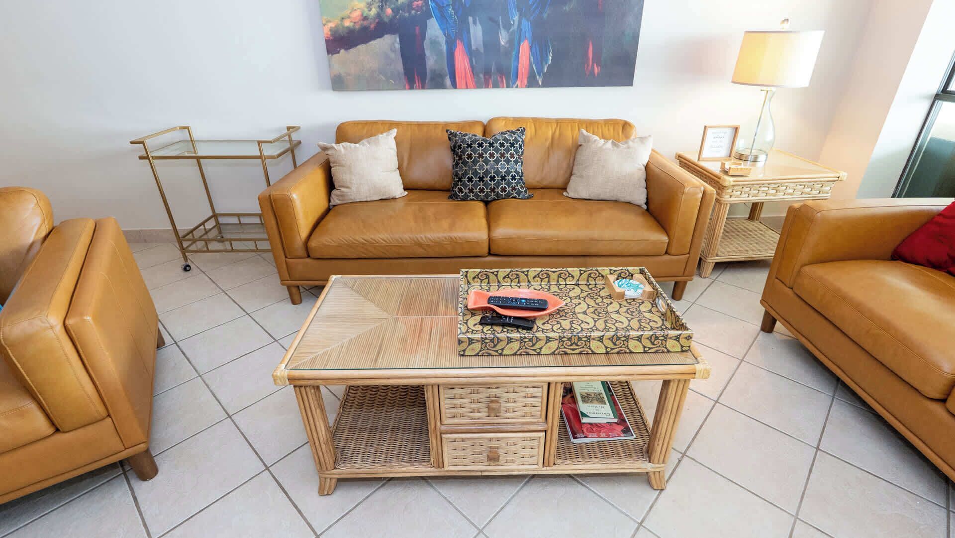 A living room with a brown leather sofa, a coffee table with a woven top, and a wall-mounted painting.