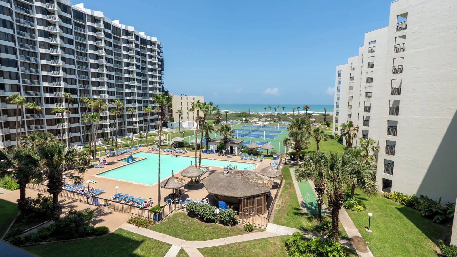 Un hotel con piscina, canchas de tenis y vistas a la playa.