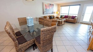 A dining area with wicker chairs, a glass table, and a painting on the wall. - Direct Beachfront 3BR - 3 Pools & 3 Jacuzzis (South Padre Island)