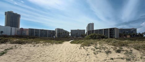 A beachfront hotel with multiple high-rise buildings, a sandy beach, and a clear sky.
