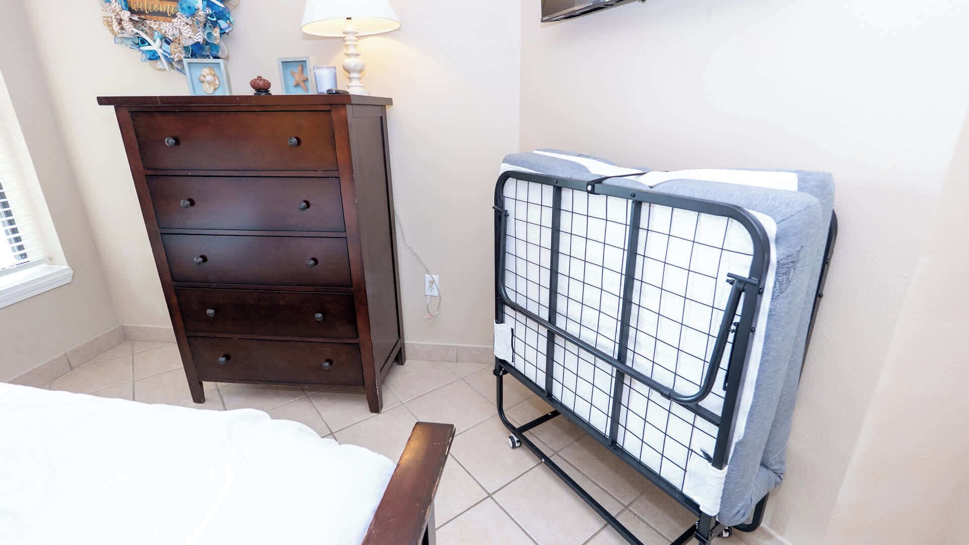 A bedroom with a wooden dresser, a metal laundry cart, and a bed.