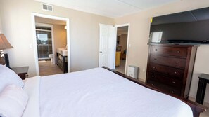 A hotel room with a bed, a dresser, a TV, and a bathroom visible through an open door. - Direct Beachfront 3BR - Access to 3 Pools & 3 Hot Tubs (South Padre Island)