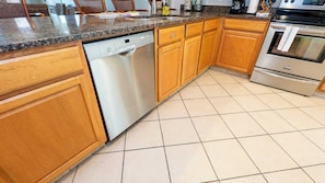 A kitchen with wooden cabinets, a dishwasher, a stove, and a tiled floor. - Direct Beachfront 3BR - Access to 3 Pools & 3 Hot Tubs (South Padre Island)
