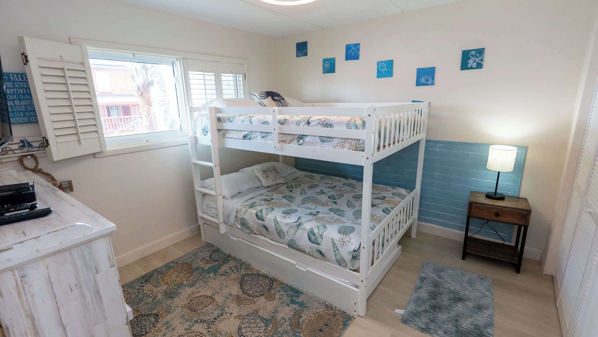 A bunk bed room with a window, a desk, a lamp, and a rug.