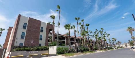 A multi-story hotel with a brick facade, balconies, and palm trees.