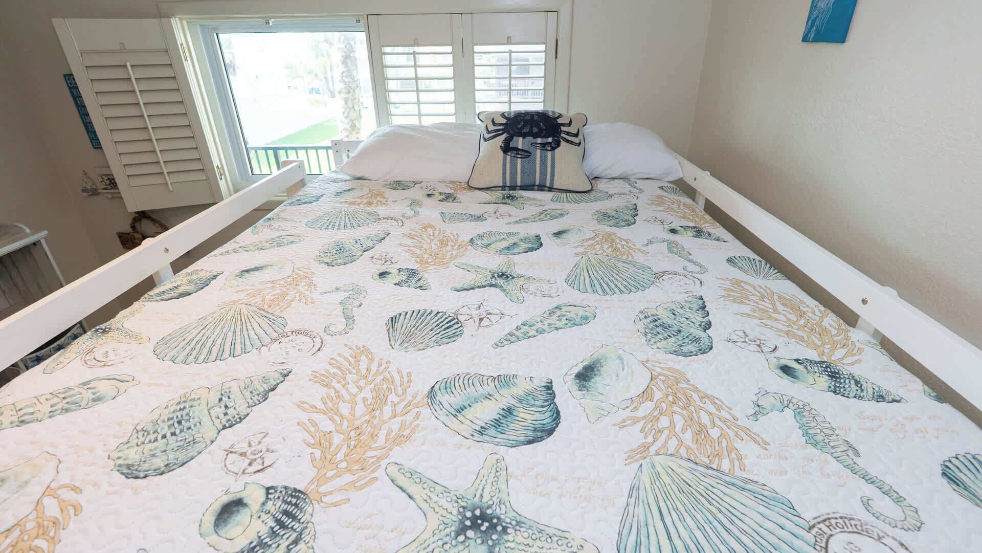 Una cama con estampado de concha marina y estrella de mar, una ventana con persianas y un adorno azul en la pared.