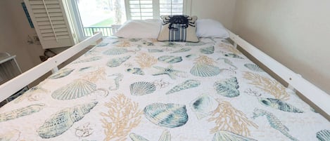 Una cama con estampado de concha marina y estrella de mar, una ventana con persianas y un adorno azul en la pared.