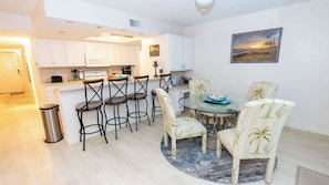 A compact kitchen with white cabinets, a bar area with stools, a dining table with chairs, and a painting on the wall. - 2BR Condo - 2 Pools - Jacuzzi - Steps to Beach SPI (South Padre Island)