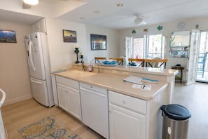 A kitchen with a refrigerator, sink, and wooden chairs. - 2BR Condo - 2 Pools - Jacuzzi - Steps to Beach SPI (South Padre Island)