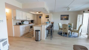 A modern kitchen with white cabinets, a central island, and a dining area with a round table and chairs. - 2BR Condo - 2 Pools - Jacuzzi - Steps to Beach SPI (South Padre Island)
