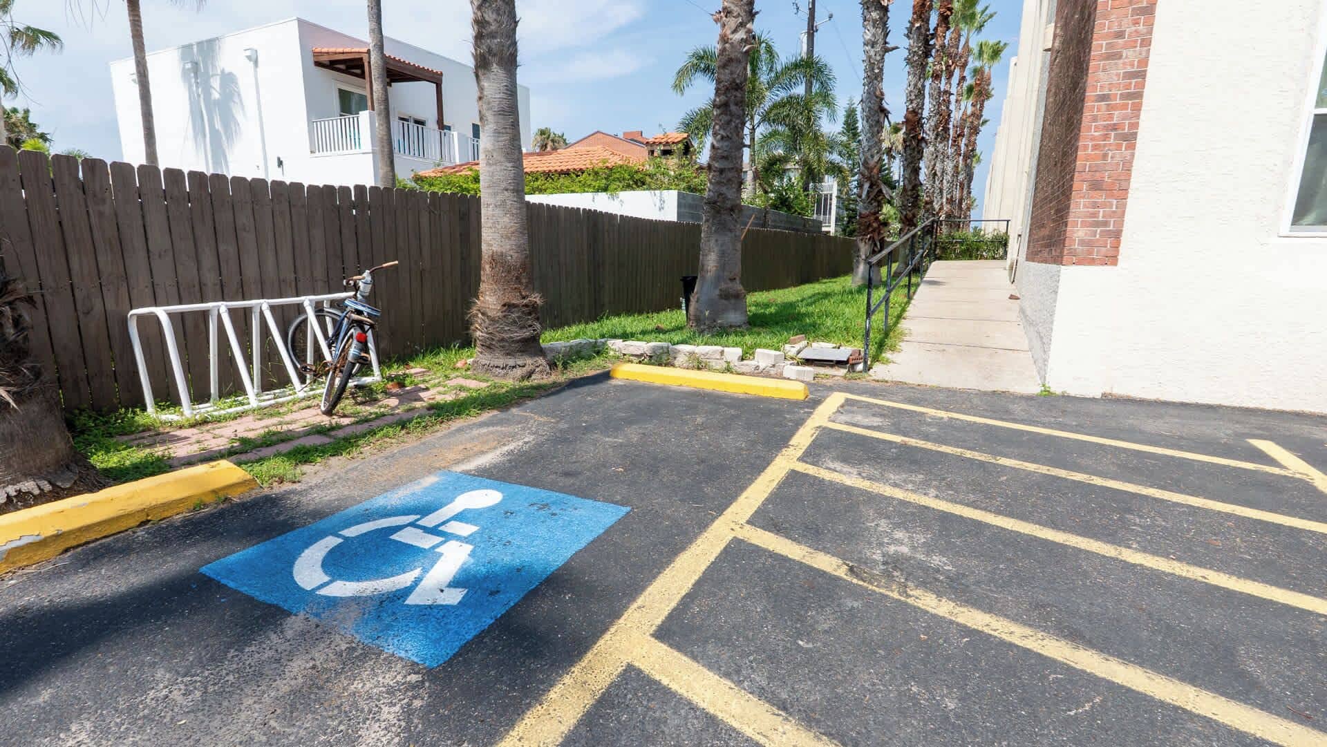 Un estacionamiento con un espacio reservado para discapacitados, una bicicleta y un edificio al fondo.