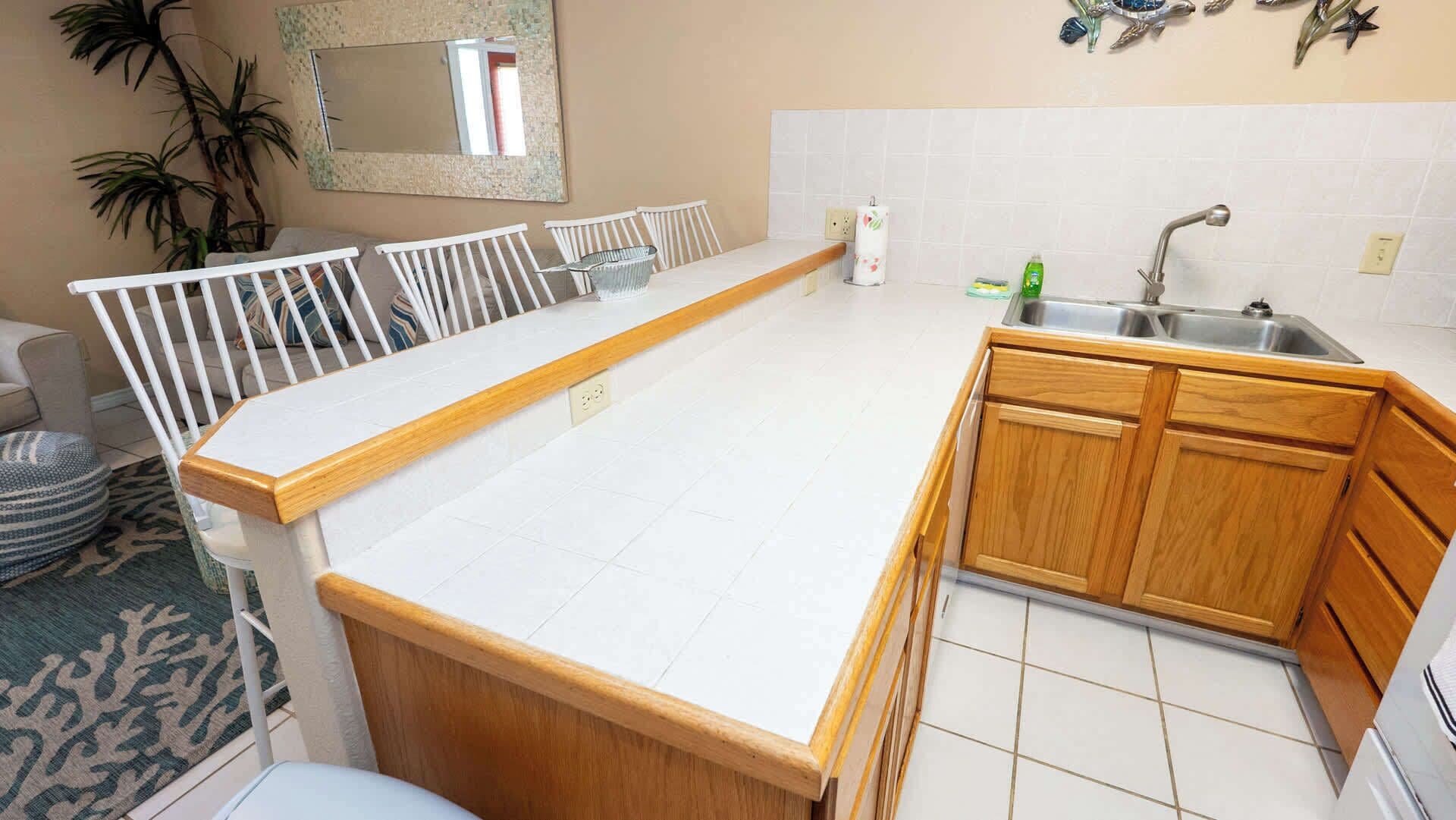 A kitchen with white countertops, wooden cabinets, a sink, and a mirror on the wall.