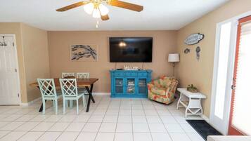 A room with a dining table, chairs, a blue cabinet, a television, and a ceiling fan.