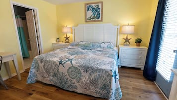 Um quarto com cama, duas mesas de cabeceira, cômoda, porta e janela com cortinas.