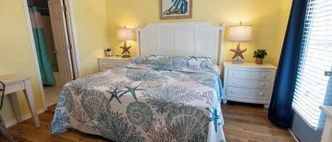 A bedroom with a bed, two nightstands, a dresser, a door, and a window with curtains.