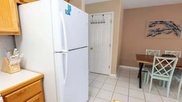 A kitchen with a white refrigerator, wooden cabinets, a dining table with chairs, and a wall-mounted art piece.