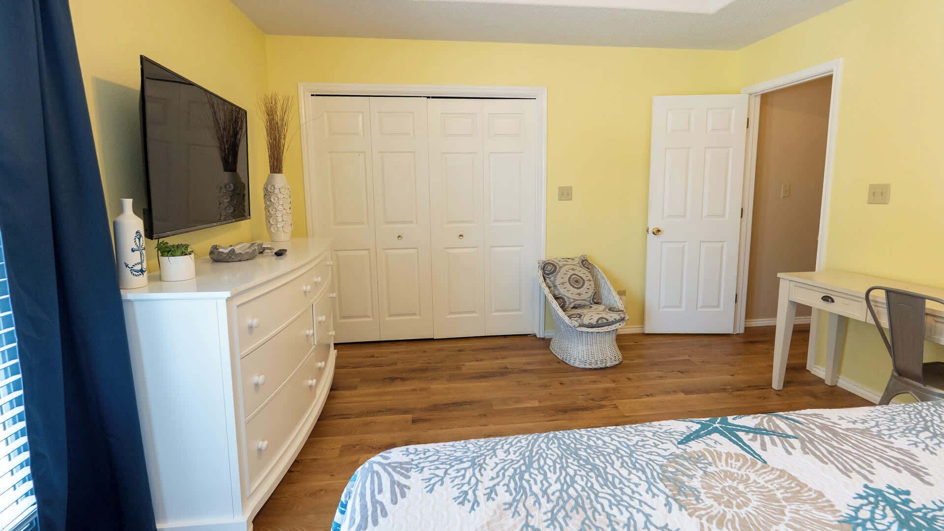 A bedroom with a bed, dresser, chair, desk, and two doors.
