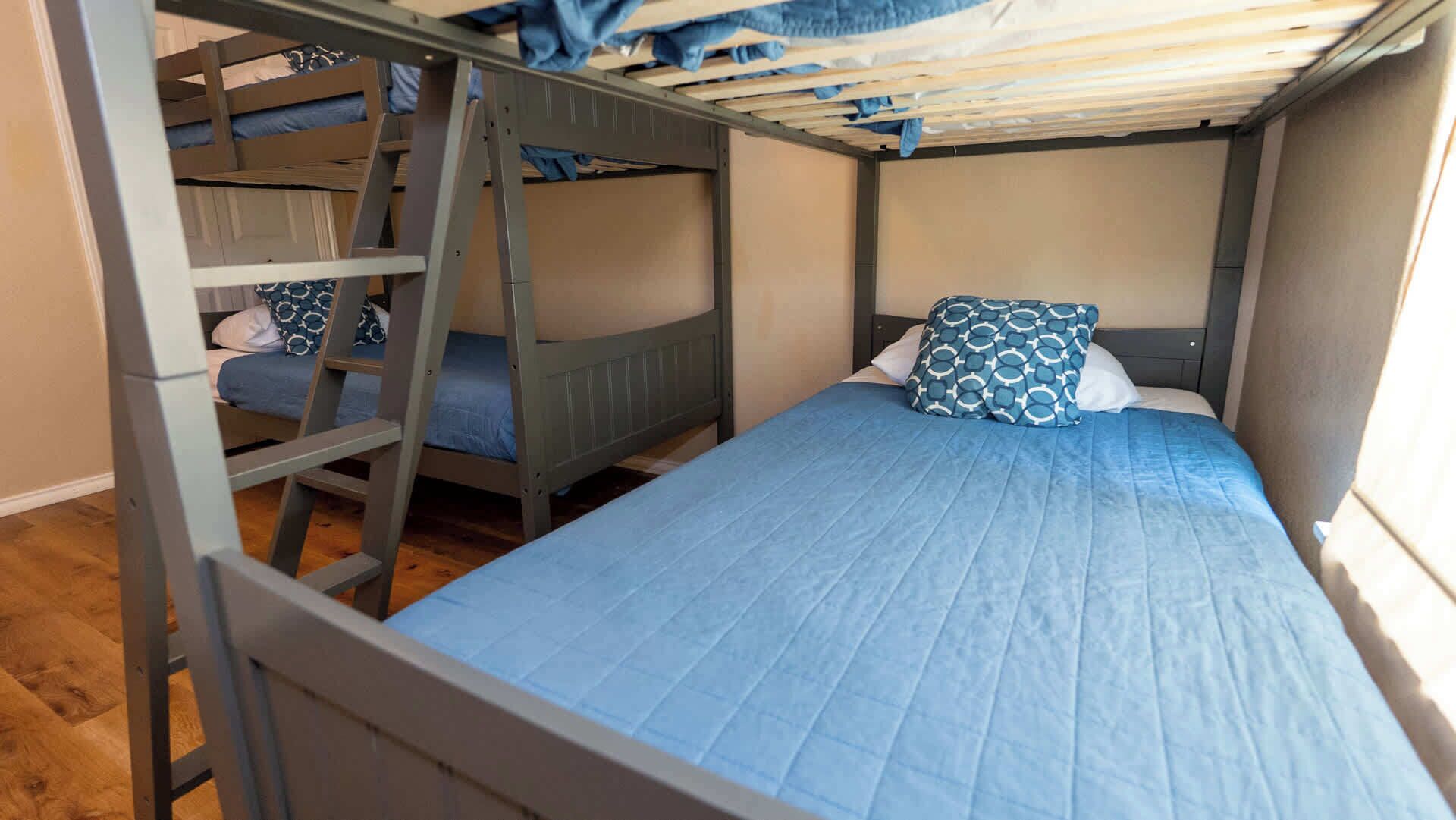 A bunk bed room with a ladder, a single bed with a patterned pillow, and a window.