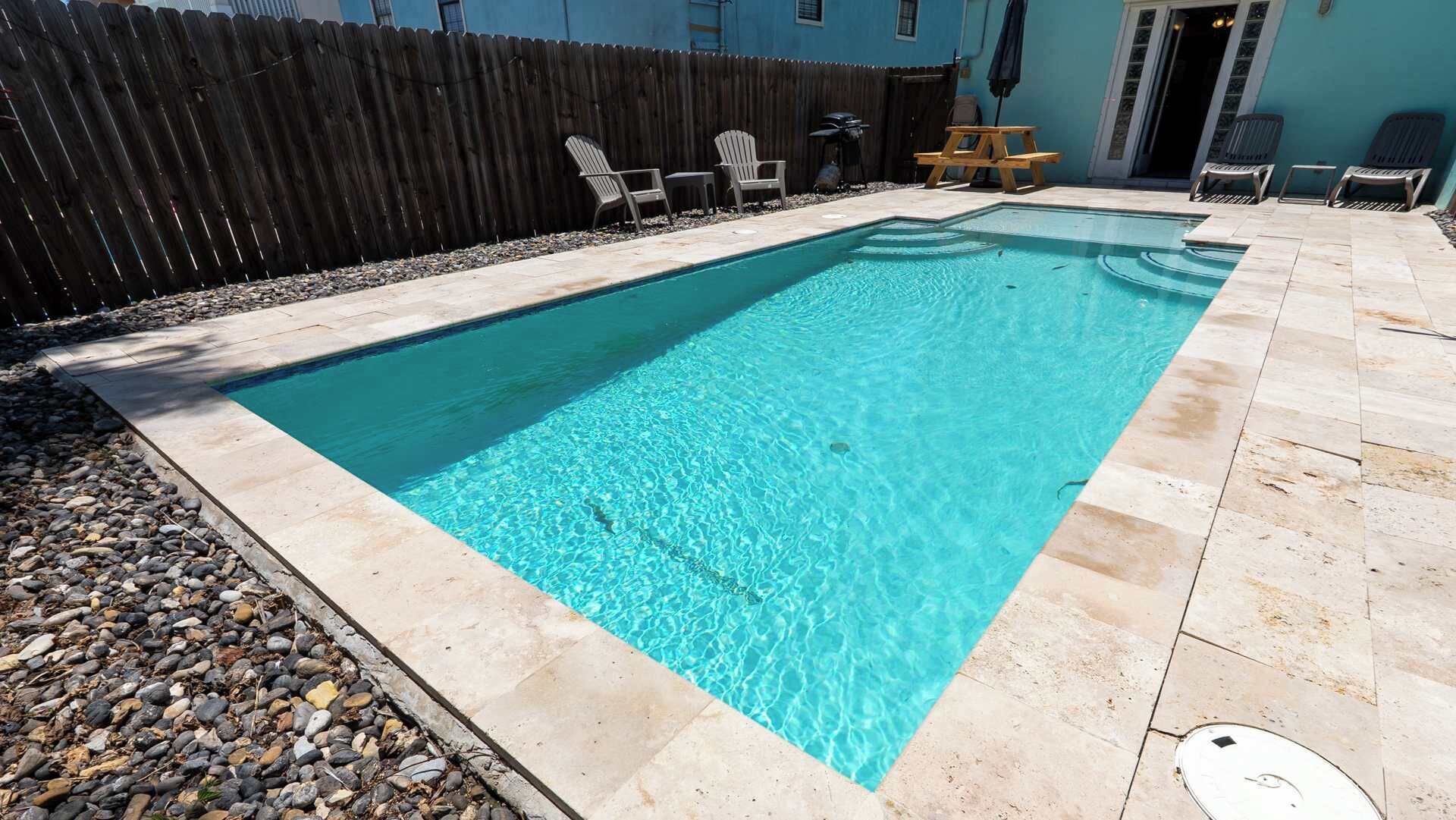 Una piscina rectangular de aguas cristalinas, rodeada por un patio de piedra y una valla de madera.