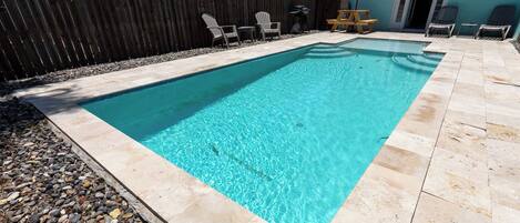 Une piscine rectangulaire à l’eau d’un bleu limpide, entourée d’une terrasse en pierre et d’une clôture en bois.