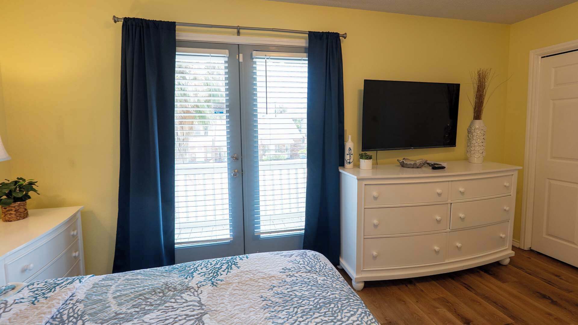 A bedroom with a bed, a dresser, a TV, and a door.