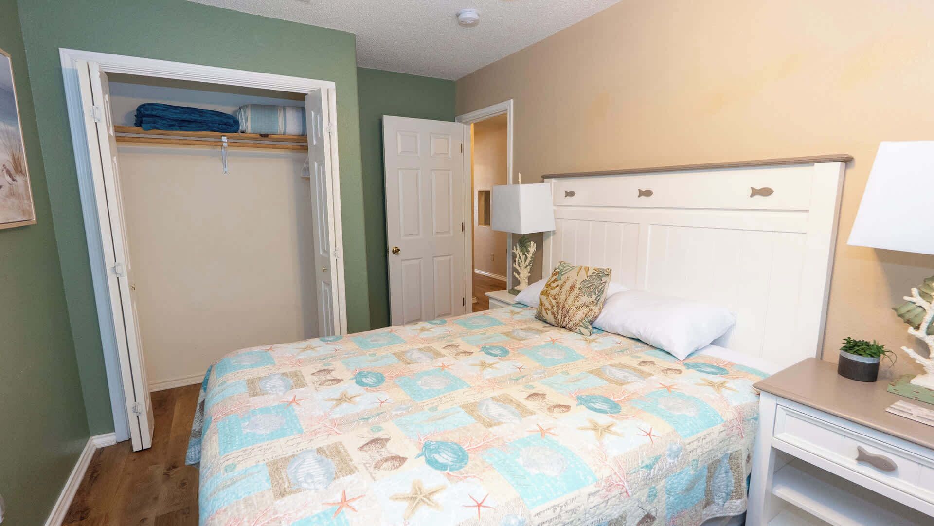 A bedroom with a bed, a nightstand, a lamp, a closet, and a door leading to another room.
