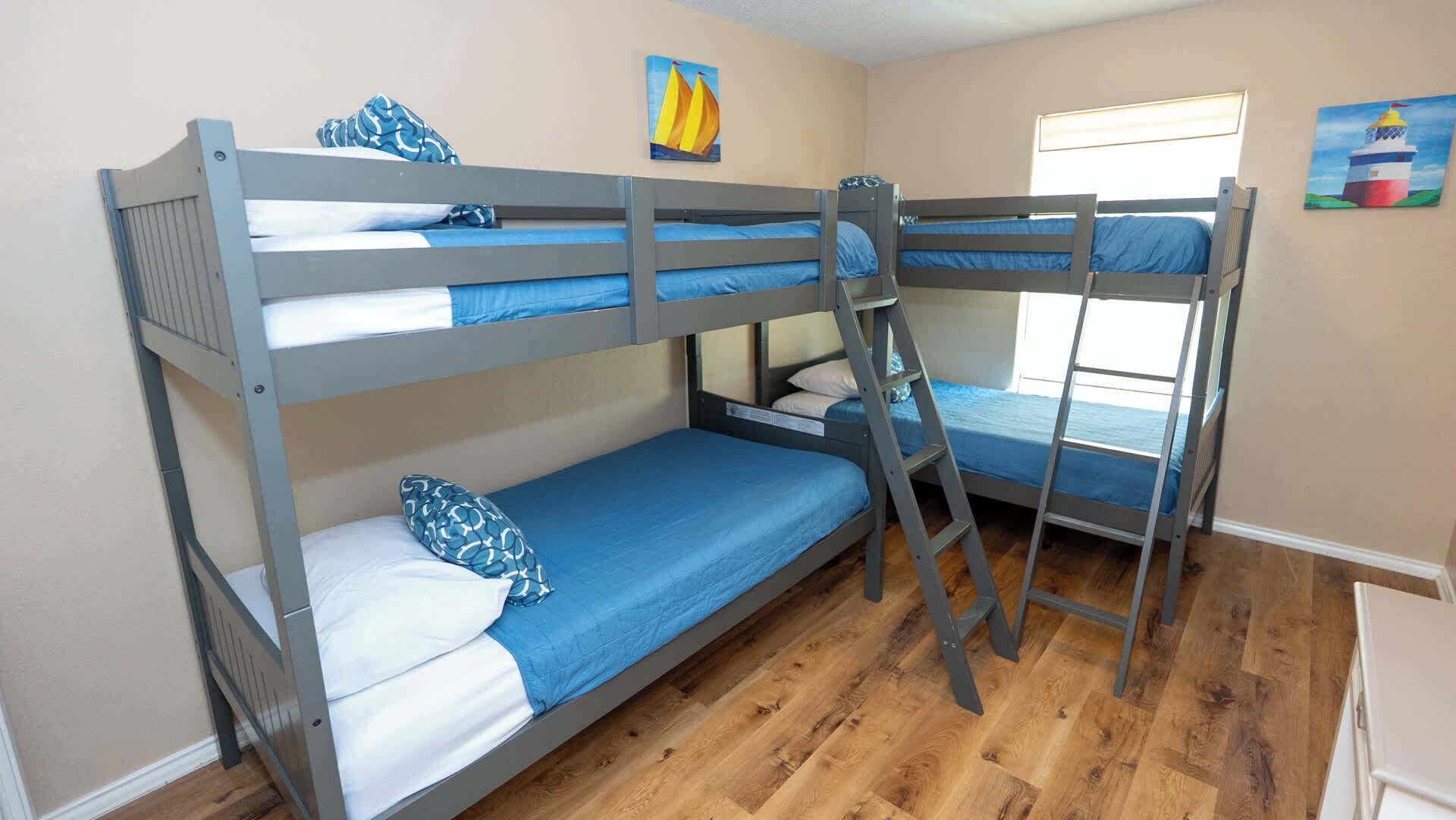 A bunk bed room with a ladder, wooden flooring, and a window.