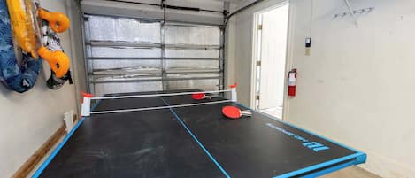 Una mesa de ping pong con borde azul, un extintor y una puerta al fondo.
