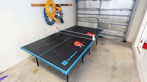 A ping pong table with two paddles, a yellow inflatable ring, and a blue and white patterned towel hanging on the wall. - New 3BR Townhome, Heated Pool, Beach Steps SPI (South Padre Island)
