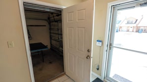 A room with a door leading to a garage, a power outlet, and a window with a view of a house. - New 3BR Townhome, Heated Pool, Beach Steps SPI (South Padre Island)