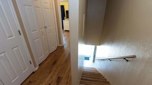 Un pasillo con puertas blancas, piso de madera y una escalera con barandilla.