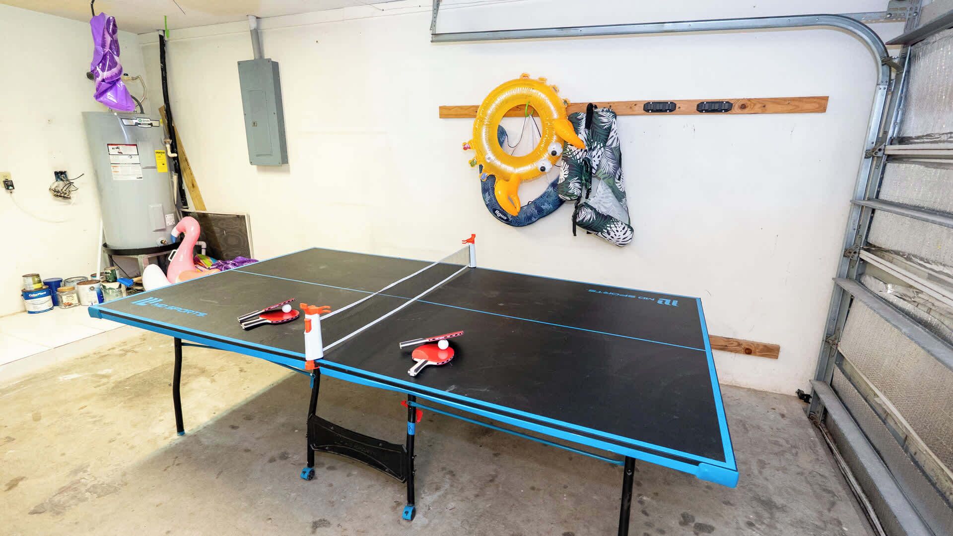 A ping pong table in a garage with a power outlet and a water heater in the background.