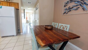 Un coin repas avec une table en bois, des chaises blanches et une décoration murale représentant des poissons.