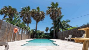 Un jardin avec une piscine, une clôture en bois et des palmiers.